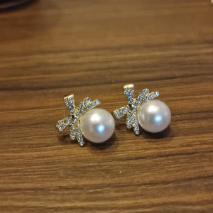 Glittriga örhängen med pärlor - Eleganta örhängen med stora vita pärlor och glittriga detaljer i form av rosett. 