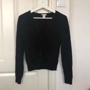 Svart kofta från H&M - Säljer en stilren svart kofta från H&M i storlek XS. Den har långa ärmar och en klassisk design som passar perfekt till både vardag och fest. Koftan är i bra skick och är en del av deras Basic-kollektion.