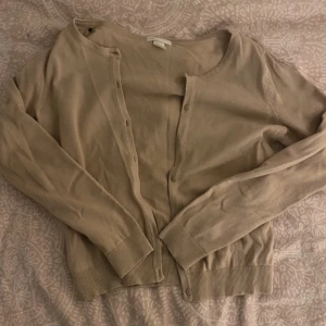 Beige kofta från H&M - Säljer en stilren beige kofta från H&M. Den har långa ärmar och knappar framtill. Perfekt för lager-på-lager och passar till många olika outfits.