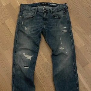 Replay jeanes - Säljer ett par snygga blå jeans från Replay med slitna detaljer. De har en klassisk femficksdesign och knappgylf. Perfekta för en avslappnad stil. W34 