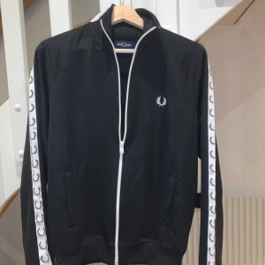 Fred Perry Tracktop - Snygg svart tracktop från Fred Perry med vita detaljer och dragkedja. Tracktopen är i toppskick och har endast använts vid 4 tillfällen. Storlek S                                                         Tröjan köptes hos Thernlunds för ca 1300kr, jag säljer en i princip ny här för 800kr.                                     Skicka PM för ytterligare bilder eller frågor!✌️
