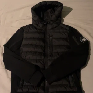 Svart pufferjacka med huva - Säljer en stilren svart pufferjacka från Peak Performance. Jackan har en praktisk huva och dragkedja framtill. Perfekt för kyligare dagar med sin quiltade design.