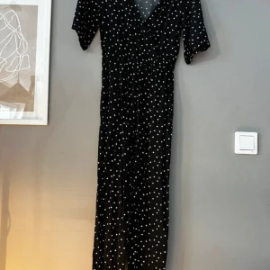 Svart prickig byxdress från Monki - Säljer en svart byxdress från Monki med vita prickar. Klänningen har en v-ringad design och korta ärmar, perfekt för en stilren look. Den är i storlek XS och passar utmärkt för både vardag och speciella tillfällen.