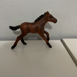Leksaks häst - En detaljerad brun hästfigur i plast med svart man och svans. Perfekt för samlare eller som leksak för barn som älskar hästar. Figuren står i en dynamisk pose som ger ett livfullt intryck.