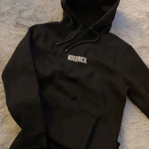 Svart hoodie från Hoodrich - Säljer en stilren svart hoodie från Hoodrich med vit logga på bröstet. Den har en klassisk känguruficka och justerbar huva med dragsko. Perfekt för en avslappnad stil, säljer den för jag inte längre använder men den är jätte fin och mysig. Pris går att diskutera💕