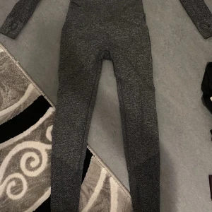 Grå träningsset med långärmad topp och leggings - Säljer ett grått träningsset som inkluderar en långärmad topp och matchande leggings. Setet är tillverkat i ett stretchigt material med ribbade detaljer och hög midja på leggingsen för extra komfort. Perfekt för träning eller en aktiv vardag.