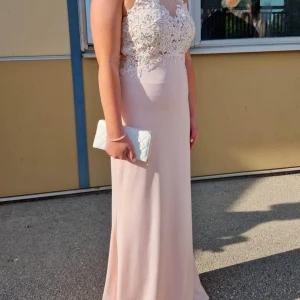 Ljusrosa balklänning med spetsdetaljer - Elegant ljusrosa långklänning med vackra spetsdetaljer på överdelen. Klänningen har en hög hals och är ärmlös, vilket ger en sofistikerad look. Perfekt för speciella tillfällen. Passade mig som är 165cm