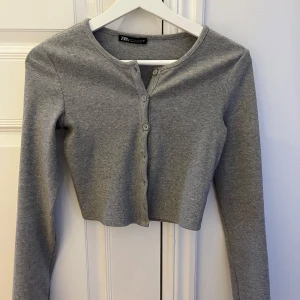 Grå ribbad kofta från Zara - Säljer en söt grå ribbad kofta från Zara. Den är croppad med knappar framtill och har långa ärmar. 