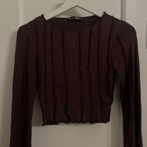 Brun långärmad topp  - Snygg brun långärmad topp med ribbade detaljer. Perfekt för en stilren look. Toppen är croppad och har en rund halsringning. Använd en gång!