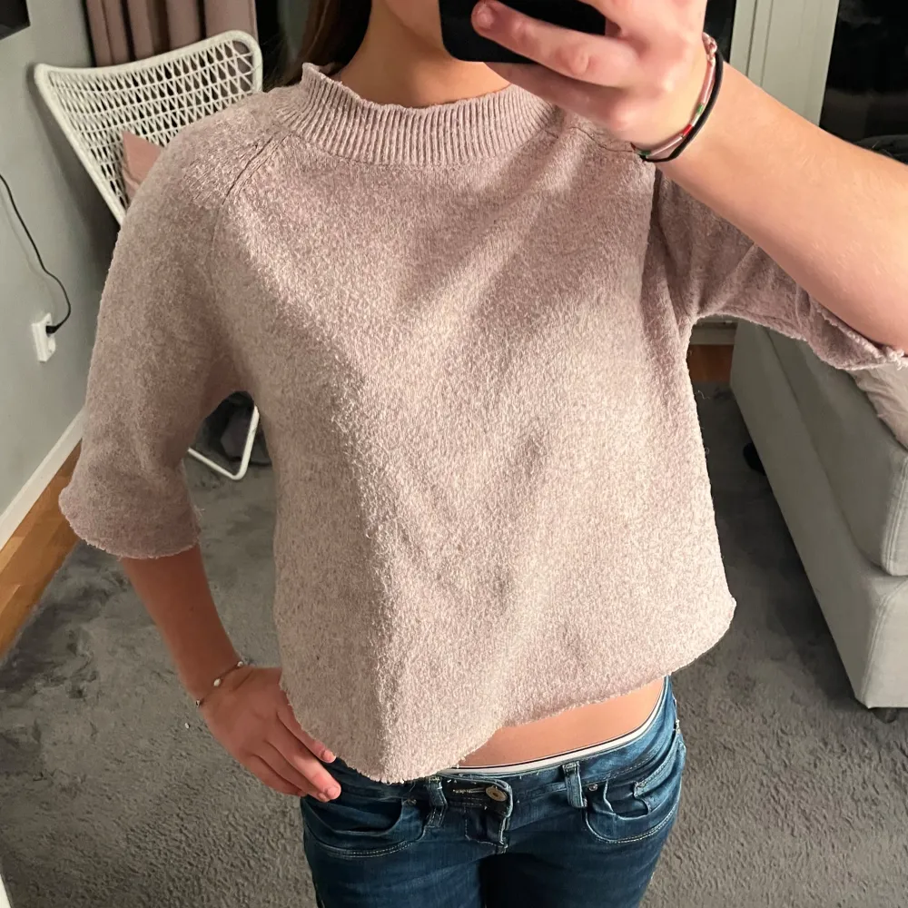 Säljer en ljusrosa/bege stickad tröja med trekvartsärm och ribbad halsringning. Tröjan är croppad och har en mysig känsla, perfekt för en avslappnad stil. Passar bra till jeans eller kjol.. Neuletakit & Villapaidat.