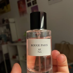 Rouge Paris Eau de Parfum - Säljer en elegant Eau de Parfum från Rouge Paris. Flaskan rymmer 50 ml och har en stilren design med svart lock och transparent glas. Perfekt för den som söker en sofistikerad doftupplevelse.