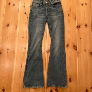 Blå bootcut jeans - Snygga blå bootcut jeans med klassisk femficksdesign och knappgylf. Perfekta för en avslappnad stil med en touch av retro. De har en lätt tvättad look som ger dem en cool vintagekänsla. Nyskick, använd fåtal gånger!