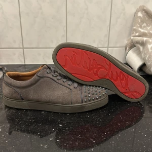 Louboutins - Snygga grå Christian Louboutins med nitar på tån och den ikoniska röda sulan. Skorna har snörning och är tillverkade i mocka, vilket ger en lyxig känsla. Har tyvärr ingen låda eller någonting med endast extra snören. Skorna är också väldigt sparsamt använda.
