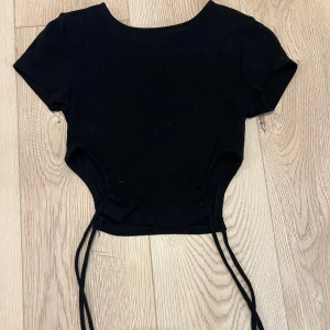 Croppad t-shirt med snören - Croppad, ribbad t-shirt men snören som man knyter i sidorna. Säljer då den är för liten.