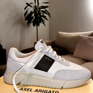 Vita sneakers från Axel Arigato - Snygga vita sneakers från Axel Arigato med svarta detaljer och snörning. Skorna har en modern design med en tjock sula och är tillverkade i en kombination av skinn och syntetmaterial. Perfekta för en stilren look.  Retail: 2600kr / 260 euro 
