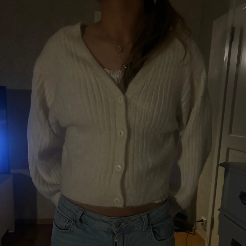 Säljer en mysig vit ribbad kofta med knappar framtill. Koftan har en croppad passform och långa ärmar, perfekt för kyligare dagar. Den är enkel att matcha med olika outfits och ger en stilren look.. Neuletakit & Villapaidat.