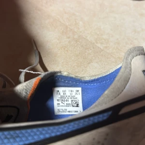 Vita fotbollsskor från Puma - Snygga vita fotbollsskor från Puma med blå detaljer och snörning. Skorna har en klassisk design med dobbar för bra grepp på planen. Perfekta för fotbollsspelare som vill ha stil och funktionalitet.