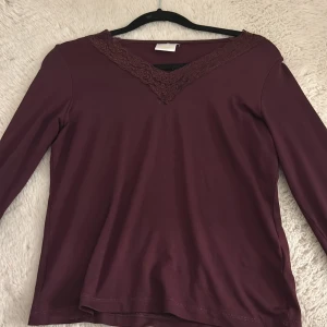 Vinröd långärmad topp med spetsdetalj - Säljer en vinröd långärmad topp med v-ringad spetsdetalj. Perfekt för en stilren look. Passar bra till både jeans och kjol. Hör av dig vid intresse!