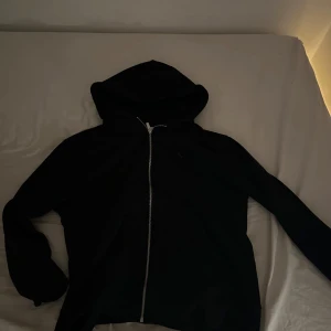 Svart hoodie med dragkedja - Säljer en svart hoodie med dragkedja och huva. Perfekt för en avslappnad stil. Den har långa ärmar och en enkel design som passar till det mesta.