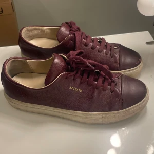 Vinröda sneakers från Axel Arigato - Snygga vinröda sneakers från Axel Arigato med guldig text. Lite slitningar vid tårna för och lite skitig sula men de går förmodligen tvätta bort. Annars bra skick!! Skriv för frågor samt prisförslag.❤️strl 37/38