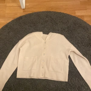 Beige kofta från Zara - Säljer en stilren beige kofta från Zara med knappar framtill. Koftan har långa ärmar och två praktiska fickor. Perfekt för en avslappnad och elegant look.
