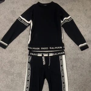 Svart tröja från Balmain - Snygg sällsynt svart tröja från Balmain med vita detaljer och logotyp längs ärmarna och midjan. Tröjan har långa ärmar och en stilren design som passar perfekt för en trendig look.