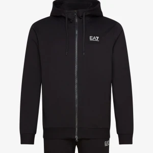 Svart hoodie från EA7 - Snygg svart hoodie från EA7 med dragkedja och huva. Perfekt för en avslappnad stil. Den har långa ärmar och en liten logga på bröstet. Passar bra till både träning och vardag. Köpt för 2200kr på Boozt har inte öppnat förpackningen och kvitto finns, kan bara mötas upp