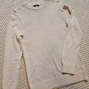 Stickad tröja - Säljer en stilren beige stickad tröja från H&M. Tröjan har långa ärmar och ribbade muddar vid ärmslut och nederkant. Perfekt för kyligare dagar.
