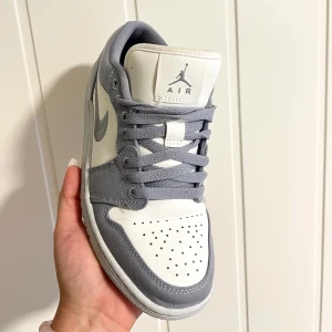 Nike Air Jordan 1 Low SE i grå och vit - Säljer ett par Nike Air Jordan 1 Low SE i en snygg kombination av grått och vitt. Skorna har en klassisk design med snörning och är i nyskick. Perfekta för både vardag och fest!