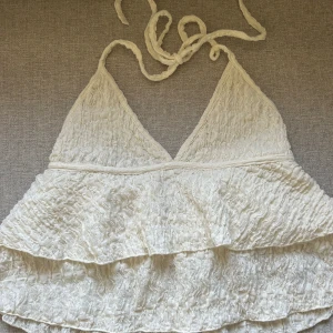 Vit volangtop från Gina Tricot - Säljer en superfin krämvit volangtop från Gina Tricot. Det är knyt i nacken och är helt oanvänd. Toppen är i ett lätt och luftigt material. 