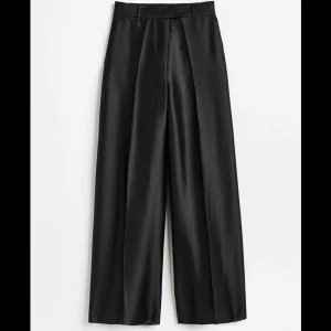 Svarta vida byxor från H&M - Säljer ett par eleganta svarta byxor från H&M i storlek 36. De är högmidjade och har en vid passform som ger en snygg siluett. Materialet ser ut att vara en glansig polyester, vilket ger en lyxig känsla. Perfekta för både fest och vardag!