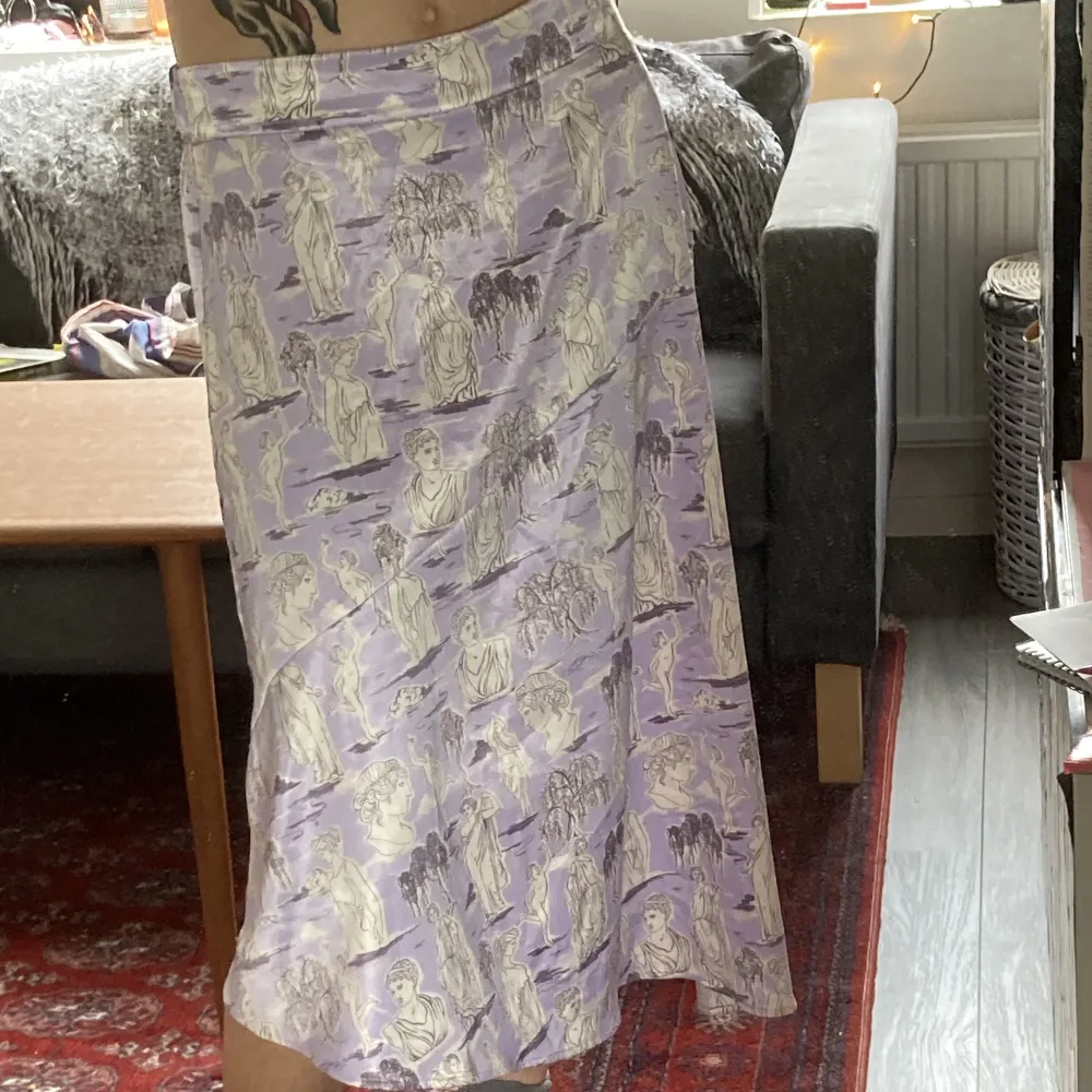 En lång mjuk och relativt tunn kjol med ett mönster av kvinnostatyer och träd. Perfekt för sommaren med det tunna tyget. Den har strech på baksidan så den sitter inte för hårt och passar fler storlekar.. Kjolar.
