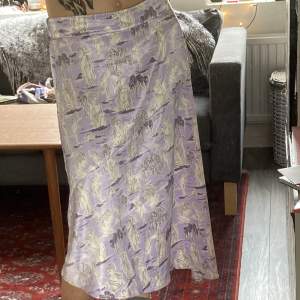 En lång mjuk och relativt tunn kjol med ett mönster av kvinnostatyer och träd. Perfekt för sommaren med det tunna tyget. Den har strech på baksidan så den sitter inte för hårt och passar fler storlekar.