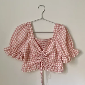 Rutig crop top - Rosa- och vitrutig crop top i bomull med lite puffärm. Går att göra längre/kortare med snöret. Storleken är ca. S eller 34-36.