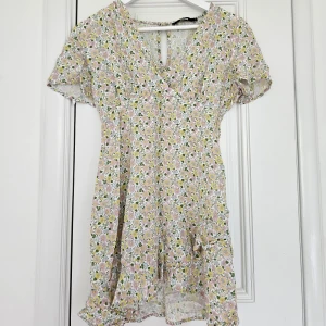 Sommarklänning  - Somrig klänning med blommor i pastellfärger💕 toppen är omlott över bröstet och nedtill är det en volang. Fint skick! 