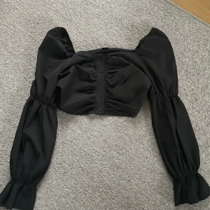 Topp - Svart topp med snygga detaljer den är även cropad. Säljer pågrund av att den inte används