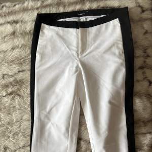 Vita byxor med svart streck från Gina Tricot i nyskick. Byxorna har fickor och dragkedja vid anklarna. Storlek 38.
