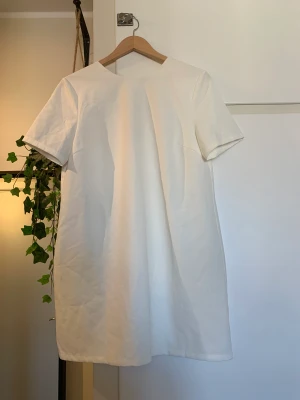 Vit t-shirt klänning  - Vit klänning med knytdetalj i ryggen. Använd 2-3 gånger. Fint tyg 