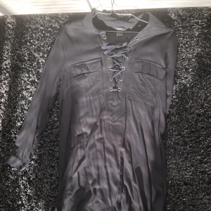 Svart klänning/tunika med knytning fram - Svart tunika/klänning från HM. Lite längre över rumpan än framme. Storlek S men passar större, kanske blir lite kort för att ha den som klänning då dock.  Kan mötas i centrala stockholm eller skickas mot frakt.