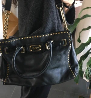 Michael Kors väska - Michael Kors väska i ok skick. Svart med guld detaljer. Den har tyvärr blivit lite missfärgad och repig undertill vilket man kan fixa om man behandlar den. Men det syns knappt eftersom det är på undersidan.