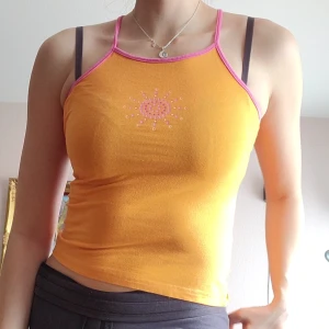 Färgglatt linne med pärlor - Inköpt mellan år 2000-2010. Gulligt Y2K linne i orange och rosa färg med tryck där fram. Har även en jättesöt dekoration med pärlor på ryggen 🧡🩷Nyskick. Svarar på alla frågor.