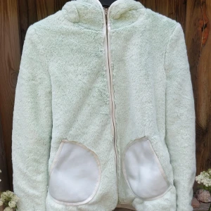 Söt fluffig jacka med öron - Supermysig och fluffig jacka med små teddybjörnöron. Liten i storlek. Plaggets längd: 63 cm Plaggets bröstvidd: 94 cm Plaggets bottenvidd: 100 cm Plaggets ärmlängd: 41 cm Kontakta mig vid frågor angående plagget och dess mått.