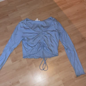 Blå långärmad som är ribbat  - Blå långärmad tröja som är ribbad som man kan knyta i mitten och även dra åt. Kortare topp.