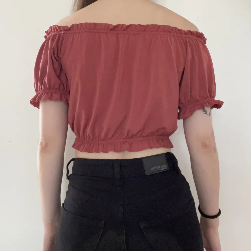 Stretchig crop top med fina detaljer från Gina Tricot i stl XS. Rosa/korallaktig färg i lite skimrigt material. Offshoulder. Fint skick då den knappt är använd. Material: 95% polyester, 5% elastan. Djur- och rökfritt hem.. Toppar.