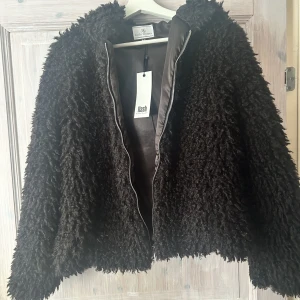 Oanvänd svart jacka med luva  - En oanvänd päls liknande svart jacka.  Kan mötas upp med jackan