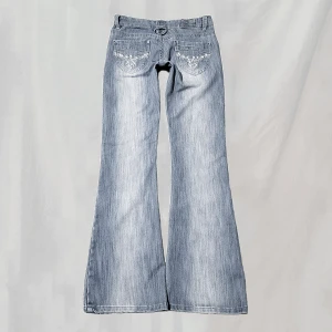 Lågmidjade jeans - Midja: 71,5 Innerben:79 Lågmidjade jeans med rhinstones. Sitter bootcut. Storlek "10", uppskattar passa en XS eventuellt S. Hittar inga uppenbara defekter. Kanske något väckade/vikta vid fotändar men överlag mycket fint skick!🤍