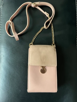 Liten mobil väska - Ganska använd och lite utnött i färgen. Men funkar fortfarande som den ska och lika snygg. Två innerfack där mobil och annat får plats. Axelband ingår. 