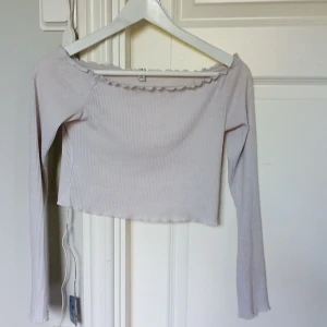 Vit långärmad tröja - Denna tröja är perfekt för personer med en mer basic/trändig stil. På andra bilden ser man en bit av plastkanten som går längst upp runt tröjan. Denna plastkant finns för att tröjan ska kunna sitta på plats tills man väljer att ta av sig den,ser ut som ny