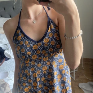 Halterneck klänning - Blå Sommarklänning med orangea blommor, köpt förra sommaren secondhand men i bra skick! Lite för stor på mig, skulle säga att den är storlek M/L. Går t knäna på mig som är 167cm. Skriv för fler bilder, pris går att diskutera!
