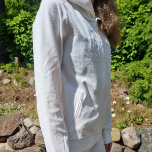 Mjukissett/veloursett - Snyggt vitt mjukissätt i velor. Huvtröja i velour med hel dragkedja, två fickor med dragkedja, luva o "wow" tryck på bröstet. Säljes tillsammans med matchande velourbyxor med en lätt bootcut. Innermått 79 cm.  Använt få gånger, är i ett mycket bra skick.